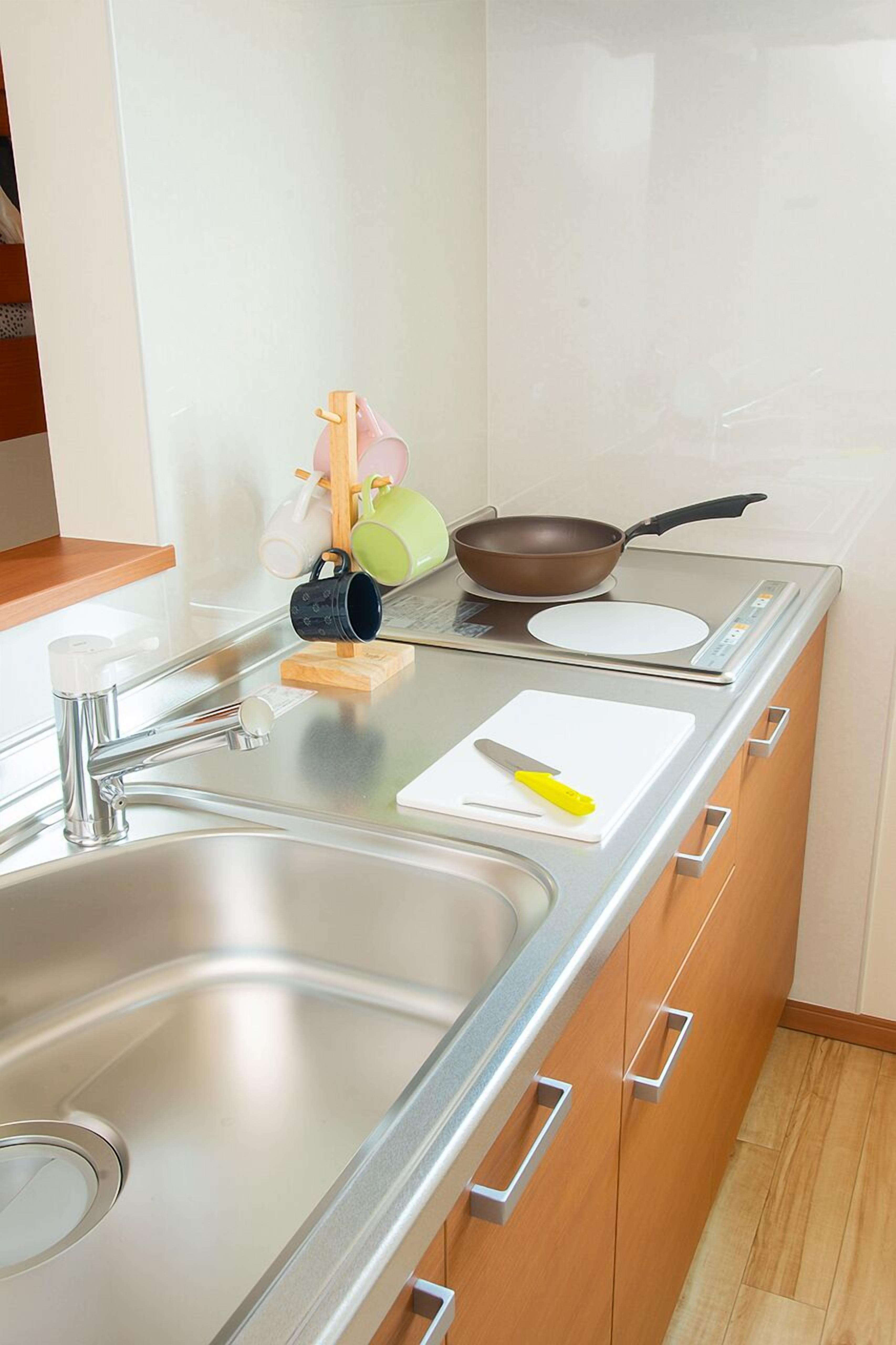A modern kitchen with a stainless steel sink, wooden cabinets, a stovetop, and a small countertop area.