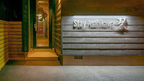 Een hotelentree met een bord waarop 'Stay Asahikawa' staat.