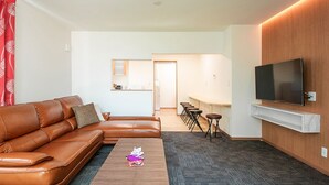 Een moderne woonkamer met een leren bank, een flatscreen televisie bevestigd aan een houten wand, en een kleine salontafel.