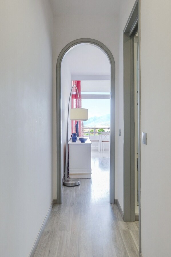 A hallway with a white door, a round table with a lamp, and a view of the sea.