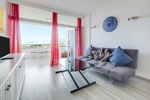 A modern living room with a sofa, a TV, and a large window with curtains.