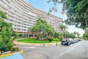 Un hôtel à plusieurs étages, doté d’une façade incurvée, d’une cour aménagée avec des palmiers et d’un parking.