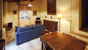 A cozy living room with a blue sofa, wooden dining table, and a kitchen area with a window and wooden cabinets. - Charming House in Tuscany with Pool & Views (Sovicille)