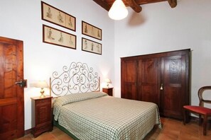 A bedroom with a bed, a wooden wardrobe, a chair, and four framed pictures on the wall. - Charming House in Tuscany with Pool & Views (Sovicille)