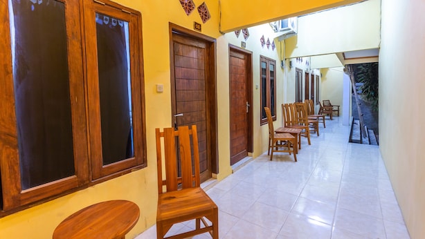 A corridor with wooden doors, a bench, and chairs arranged along the wall. - OYO 1323 Murni Homestay (Senggigi)