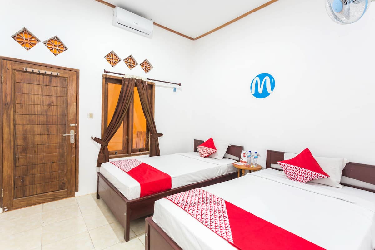 Habitación de hotel con dos camas, una puerta de madera, un aire acondicionado y un ventilador de pared.