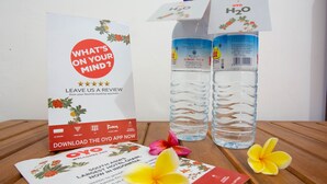 A brochure for OYO, a hotel chain, with a water bottle and a flower on a wooden table. - OYO 1323 Murni Homestay (Senggigi)