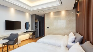 A modern hotel room with a flat-screen TV, a desk with a chair, a bed with white linens, and a wooden panel wall. - Noble Stay Hotel (Gwangju)