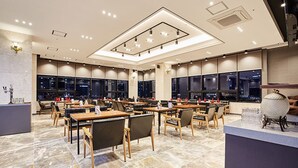 A modern hotel lobby with marble flooring, wooden tables and chairs, a reception desk, and large windows offering city views. - Noble Stay Hotel (Gwangju)