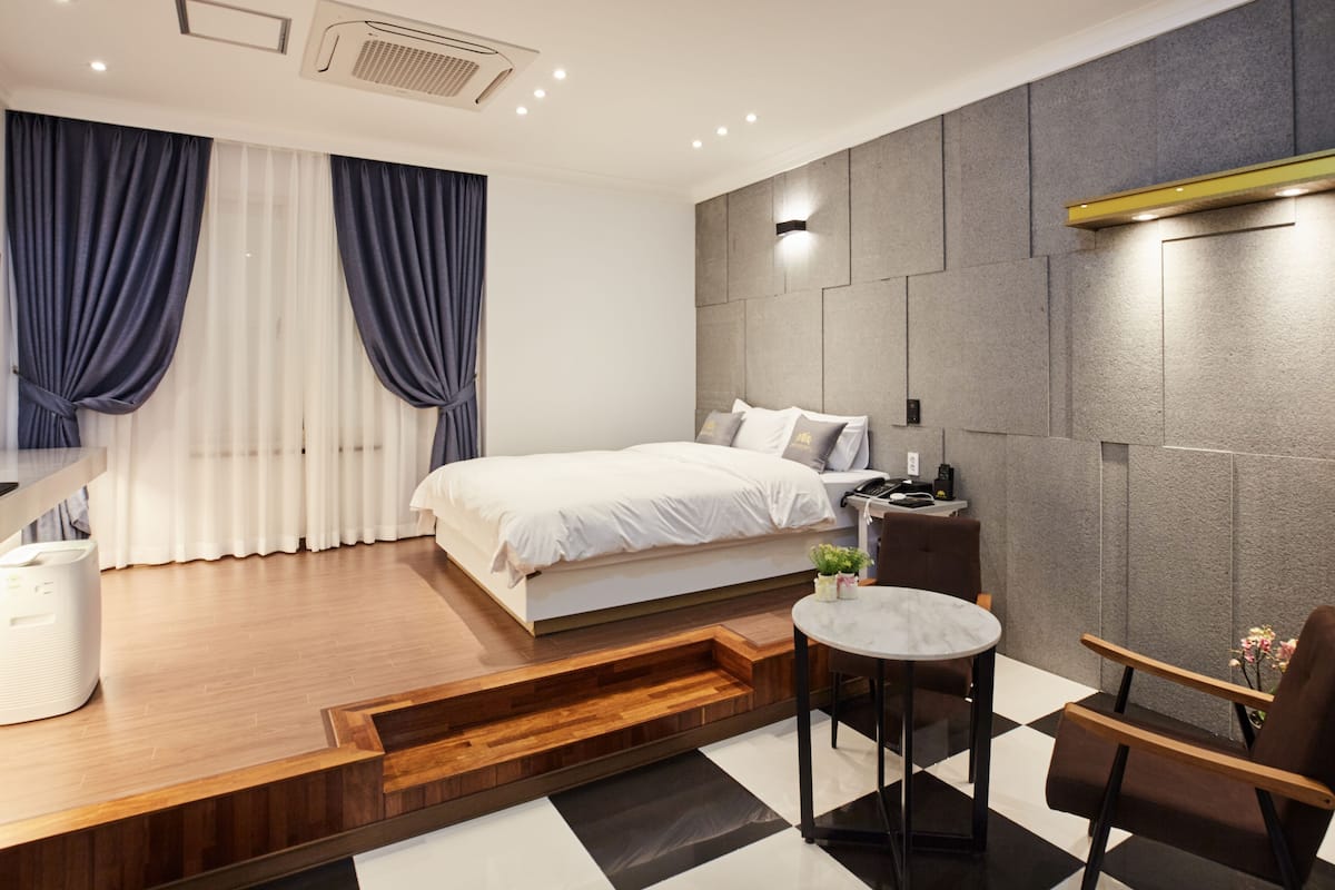 A modern bedroom with a bed, bedside table, chair, and a small round table.