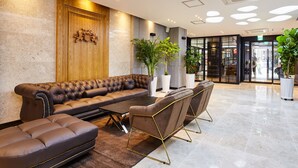 A modern lobby with a leather sofa, chairs, and potted plants. - Noble Stay Hotel (Gwangju)