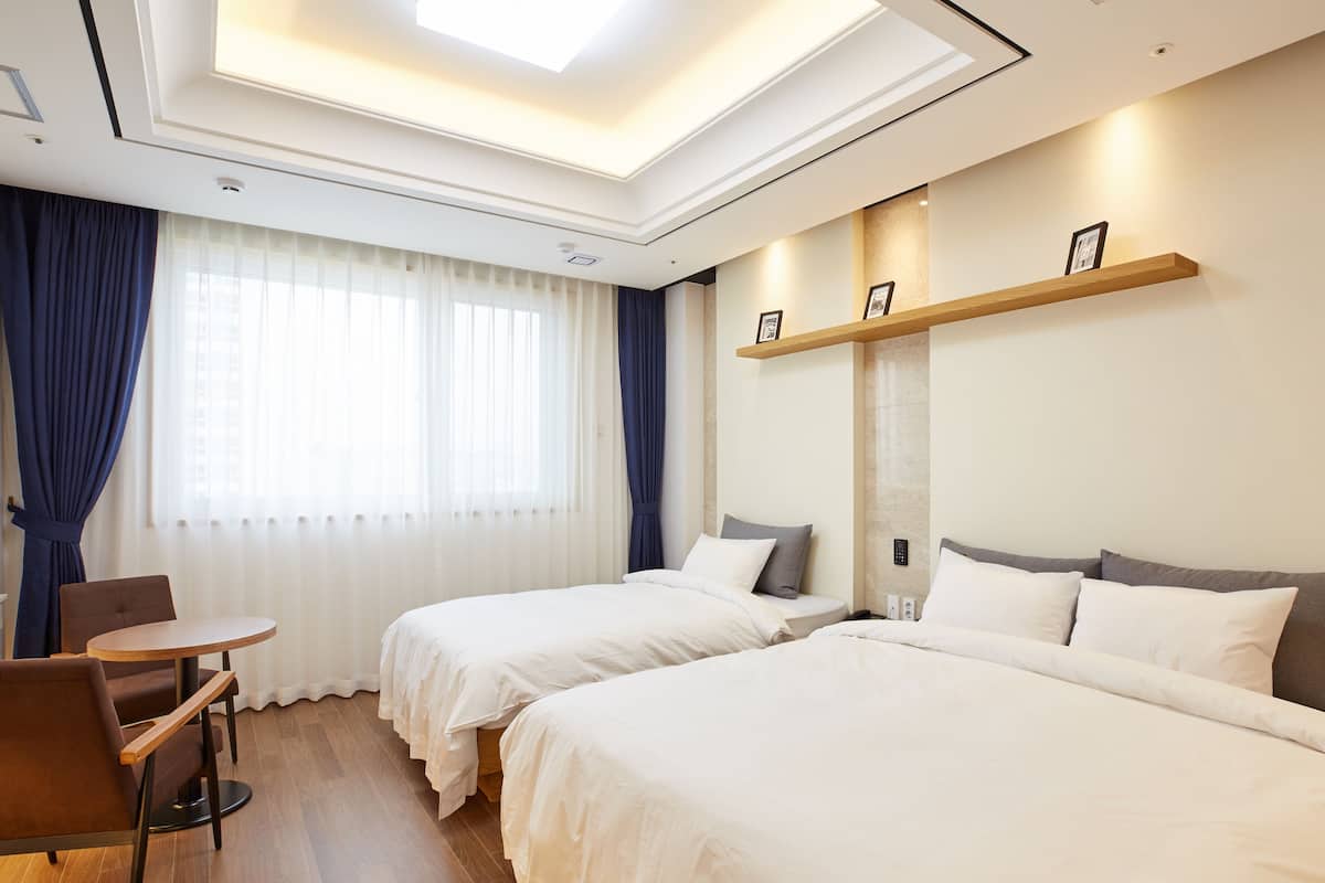 A hotel room with two beds, a small table, and a chair.