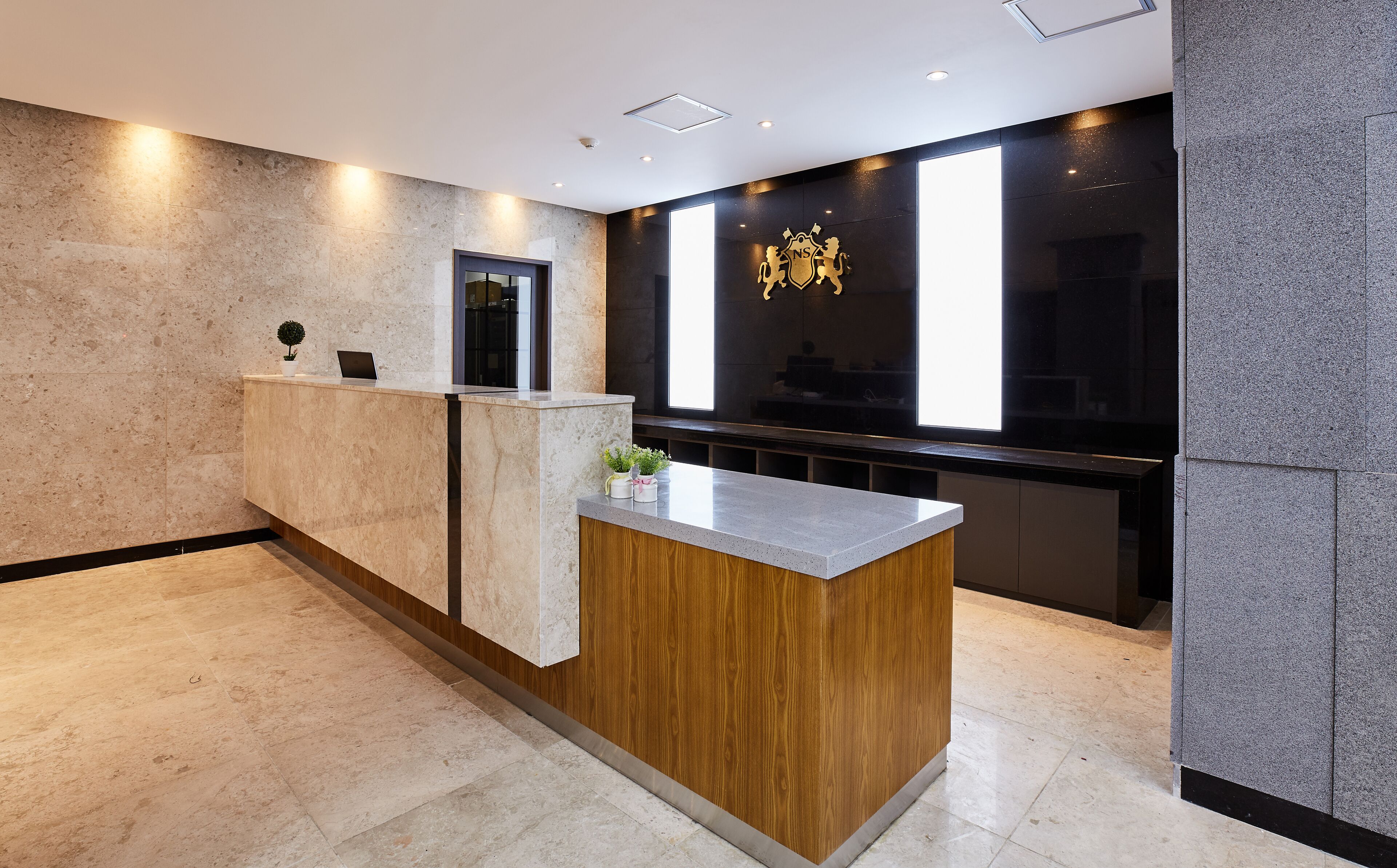 A reception desk with a wooden accent, a laptop, and a small plant.