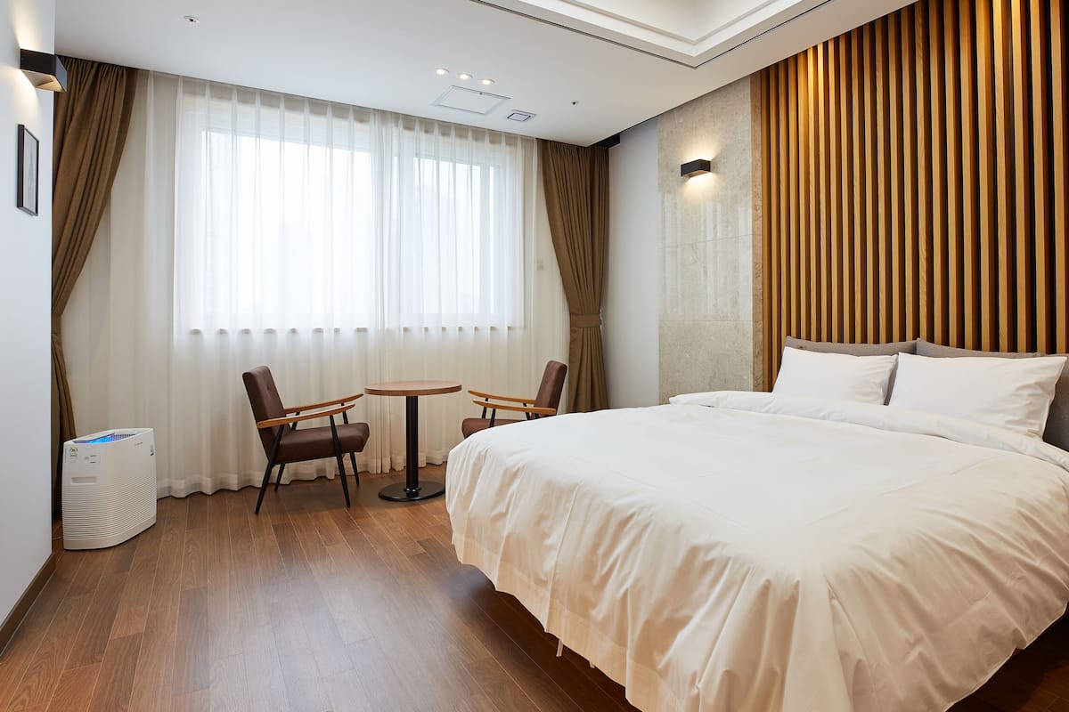 A hotel room with a large bed, two chairs, a small table, and a wall-mounted air conditioner.