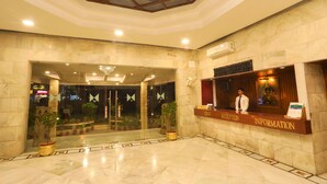 Zona de recepción de un hotel con suelo de mármol, mostrador de recepción y plantas en macetas.