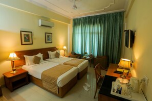 A hotel room with two beds, a desk with a lamp, a TV, and a window with curtains.