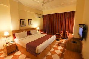 A hotel room with a large bed, a desk with a TV, a chair, and a lamp.