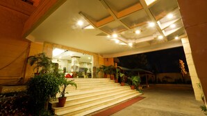 Entrada de hotel con una escalera que conduce al vestíbulo, rodeada de plantas en macetas y un interior bien iluminado.