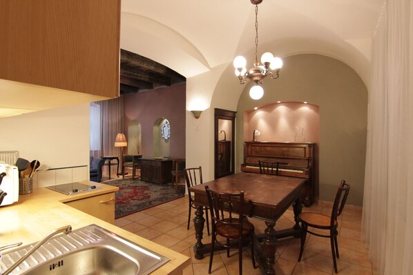 A dining area with a wooden table and chairs, a chandelier, and a kitchen area with a sink and stove.