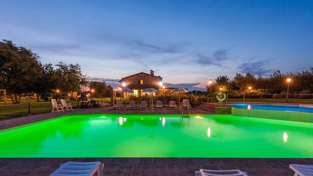 Une piscine éclairée de lumières vertes, des chaises longues et un bâtiment en arrière-plan.