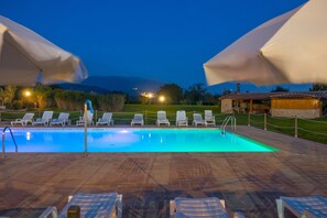 A swimming pool with lounge chairs and umbrellas, surrounded by a stone deck and a view of distant hills. - Agriturismo il Cantico di San Francesco (Assisi)
