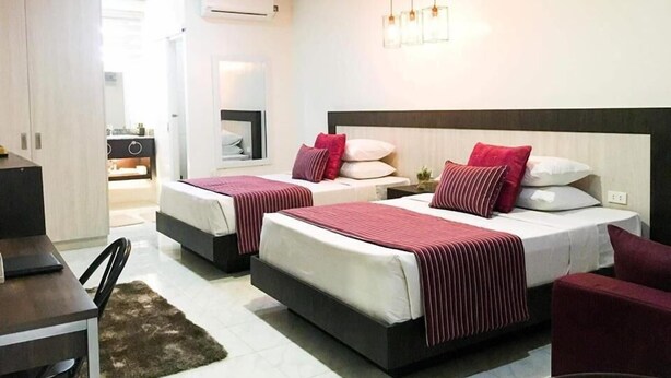 Quarto de hotel com duas camas, uma mesa, uma cadeira, televisão e armário.