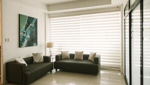 Uma sala de estar moderna com dois sofás escuros, um abajur e uma grande janela com persianas.
