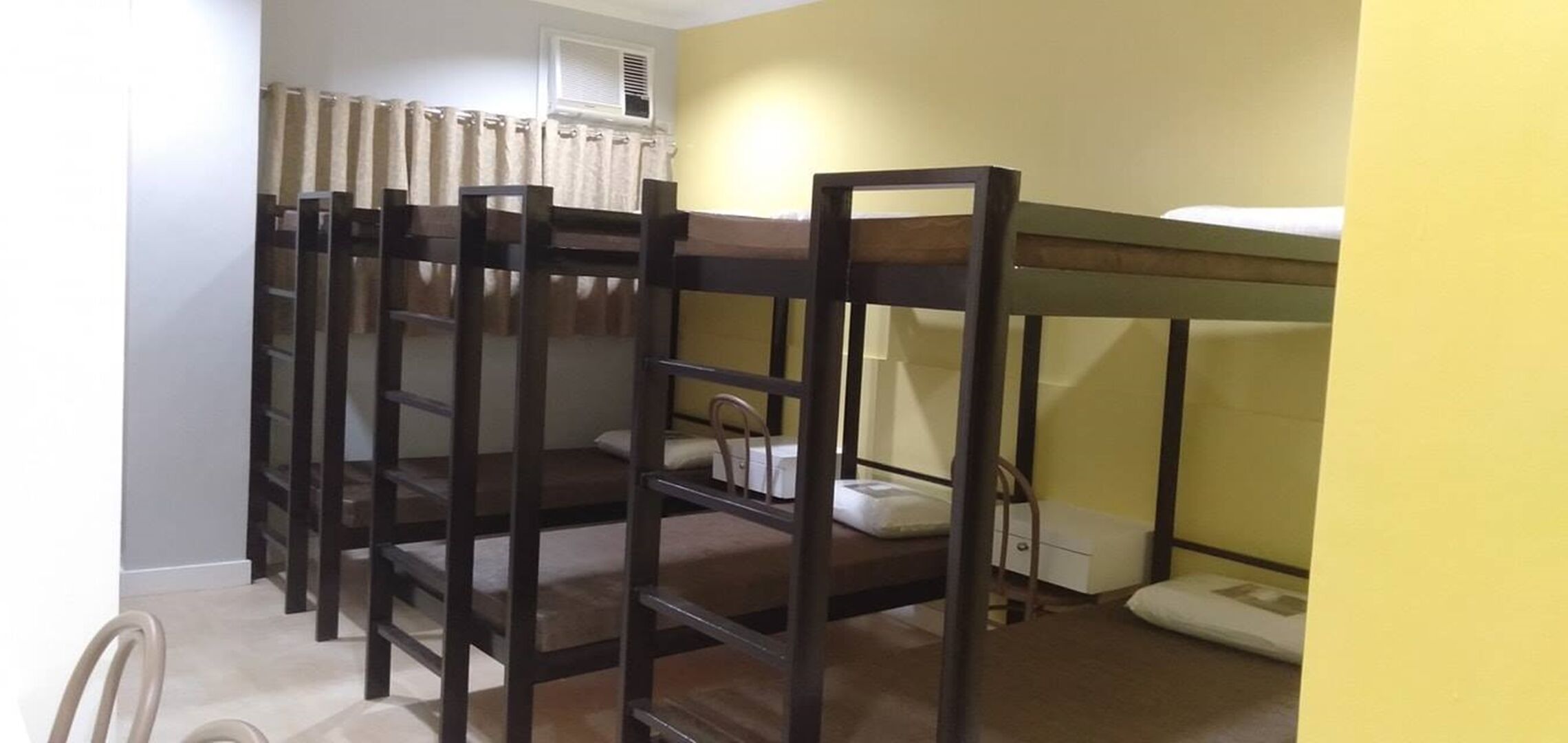 A bunk bed room with a curtain, a bedside table, and a chair.