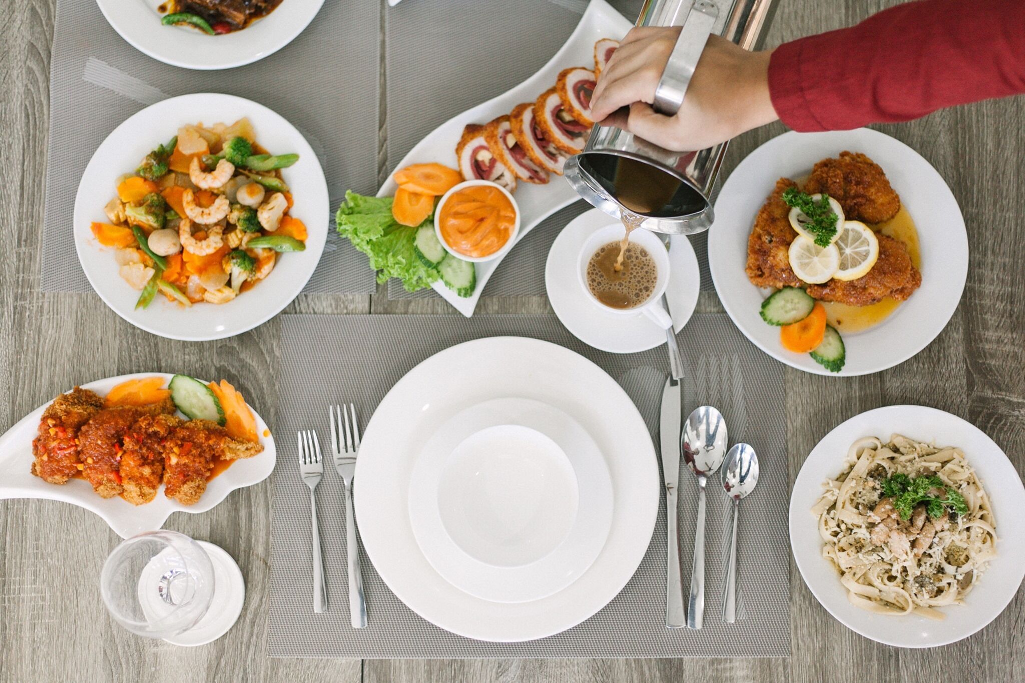 Een gedekte tafel met diverse gerechten, waaronder een vleesgerecht, groenten en pasta.