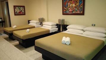 A hotel room with two single beds and a larger bed, each with towels. There are two paintings on the walls.