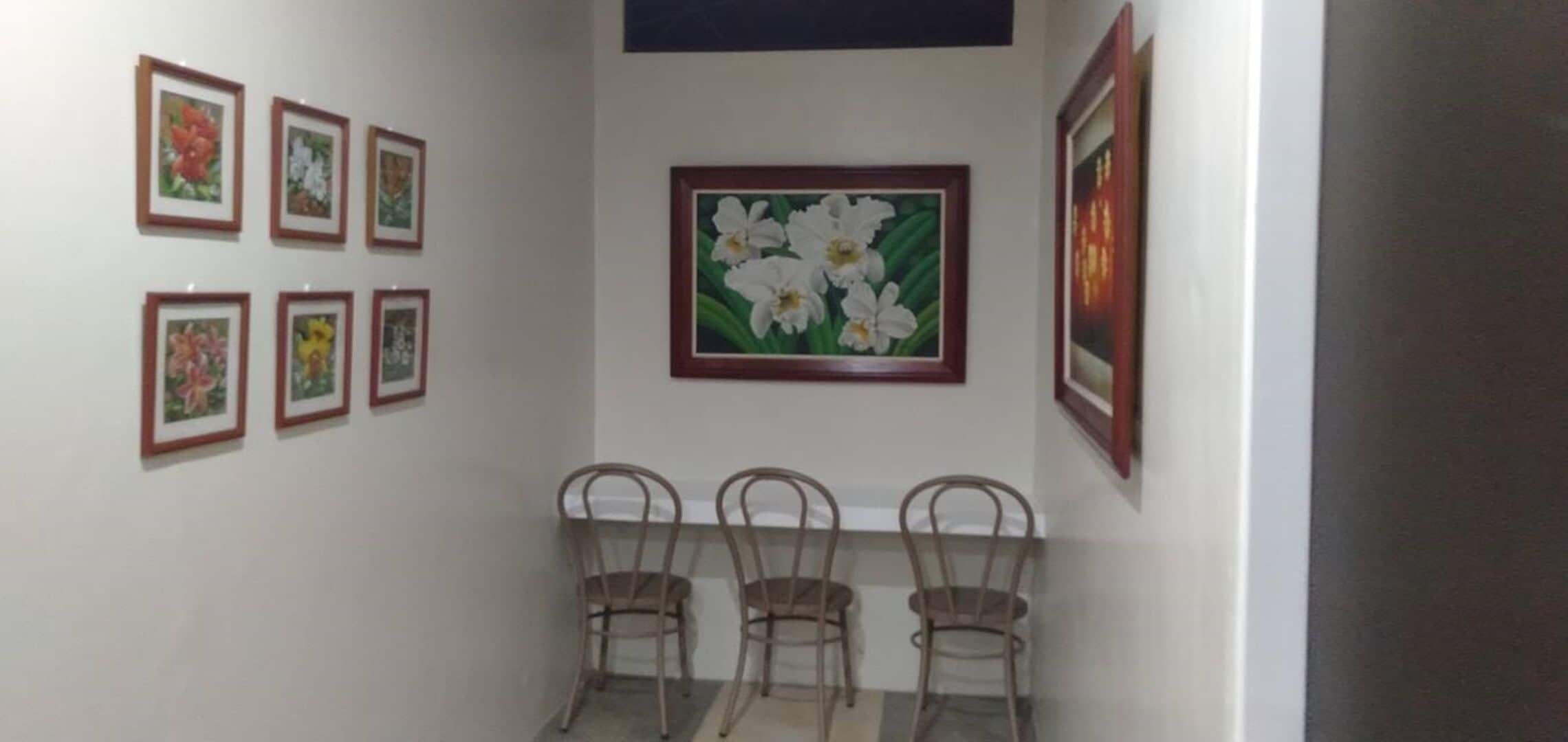 Ein Zimmer mit Essbereich, ausgestattet mit einem Tisch und drei Stühlen, einer Wand mit sechs gerahmten floralen Bildern und einem großen gerahmten Gemälde über dem Tisch.