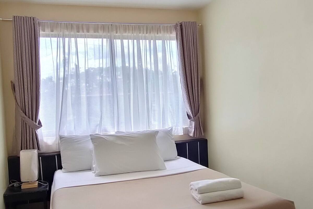 Ein Hotelzimmer mit einem großen Bett, einem Nachttisch, einer Lampe und einem Fenster mit Vorhängen.