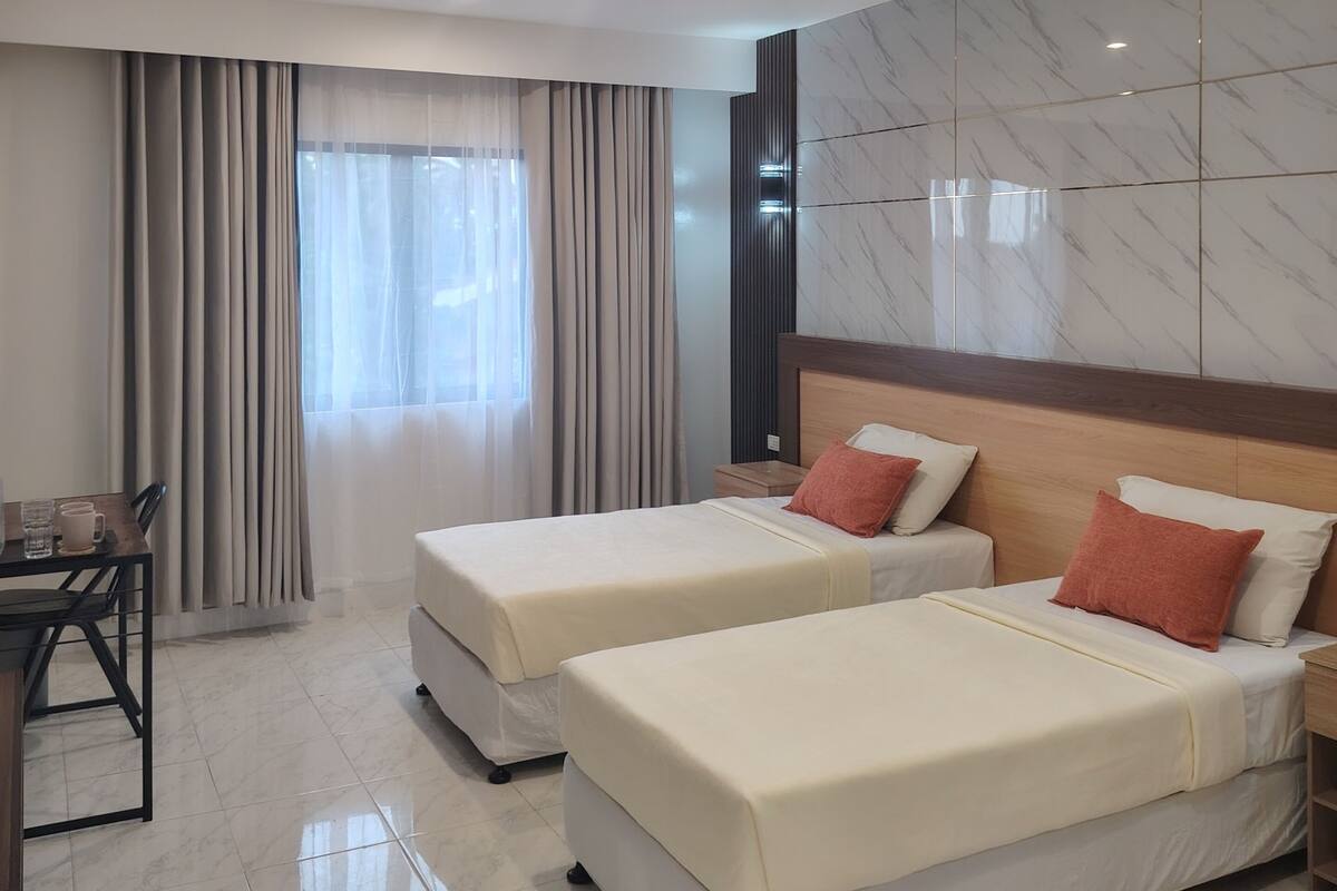 Ein Hotelzimmer mit zwei Betten, einem Schreibtisch und einem Fenster mit Vorhängen.