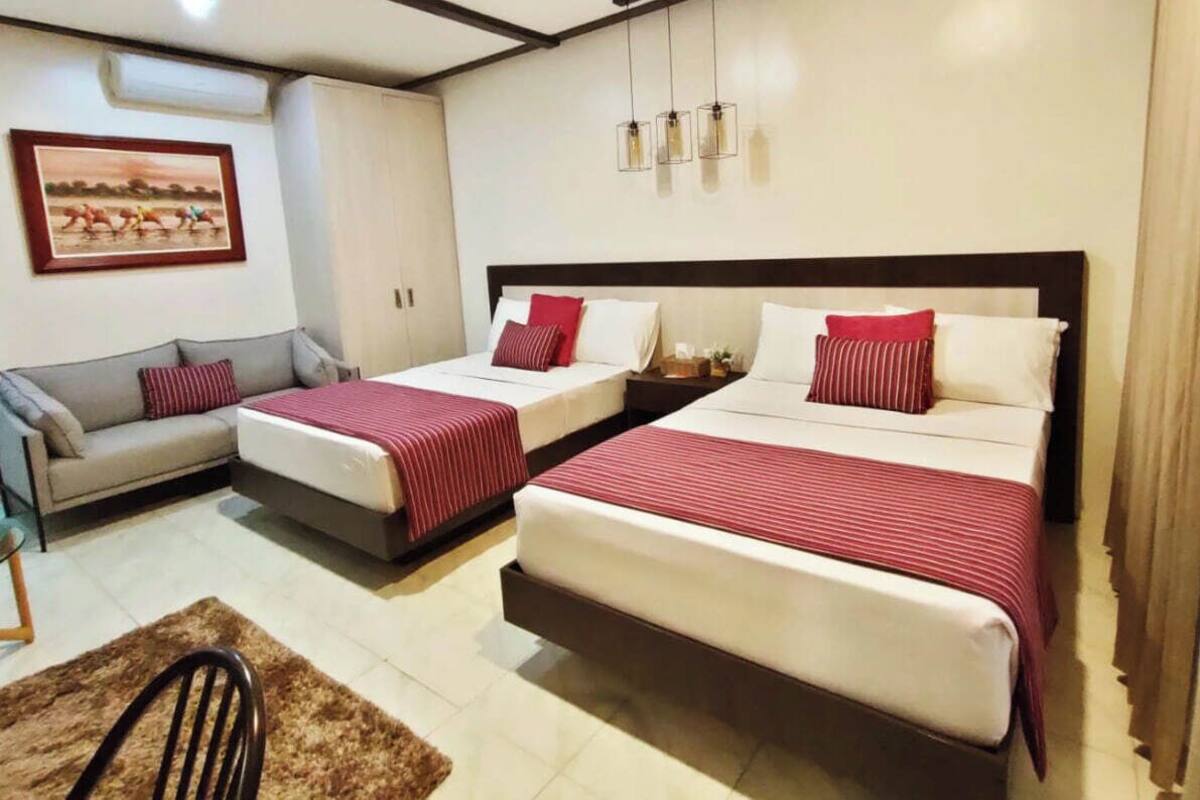 Ein Hotelzimmer mit zwei Einzelbetten, einem Schlafsofa, einem kleinen Tisch und einem gerahmten Bild an der Wand.