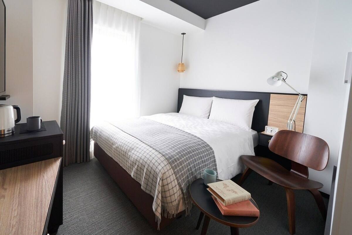 Ein Hotelzimmer mit Bett, Nachttisch, Stuhl, Lampe und einem kleinen Tisch mit Büchern.