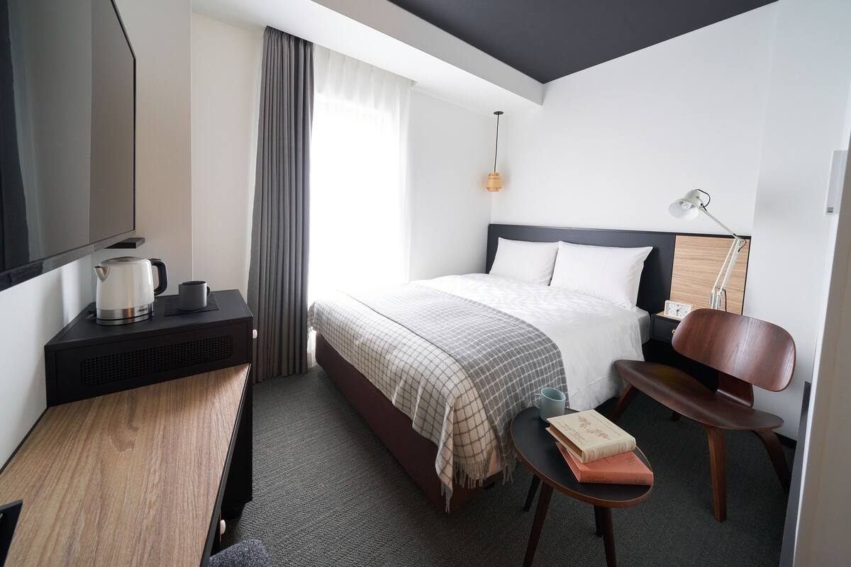 Ein modernes Hotelzimmer mit Bett, Nachttisch, Lampe und Blick auf die Stadt.