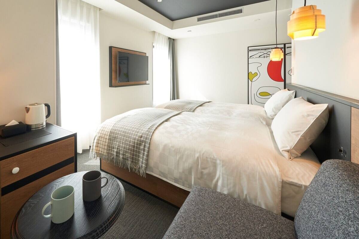 Ein Hotelzimmer mit Bett, Nachttisch, Lampe, Uhr und einem kleinen Tisch mit einer Tasse.