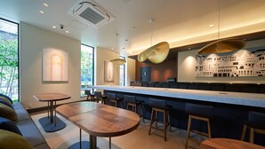 A modern bar area with wooden tables and bar stools, a large counter, and artwork on the walls. - Hotel Resol Ueno (Tokyo)