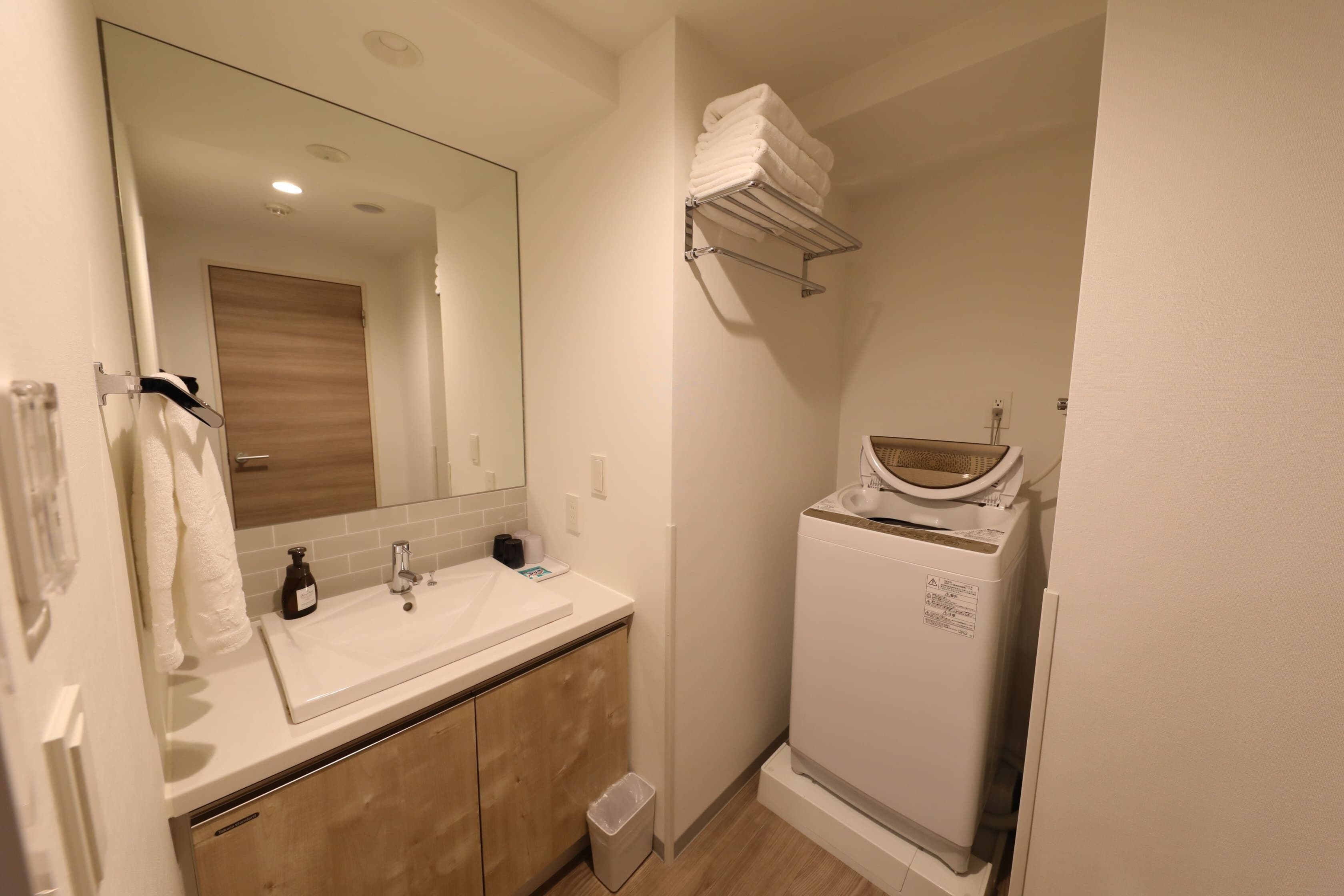 Un baño moderno con un espejo grande, un lavabo blanco, armarios de madera y una lavadora integrada.