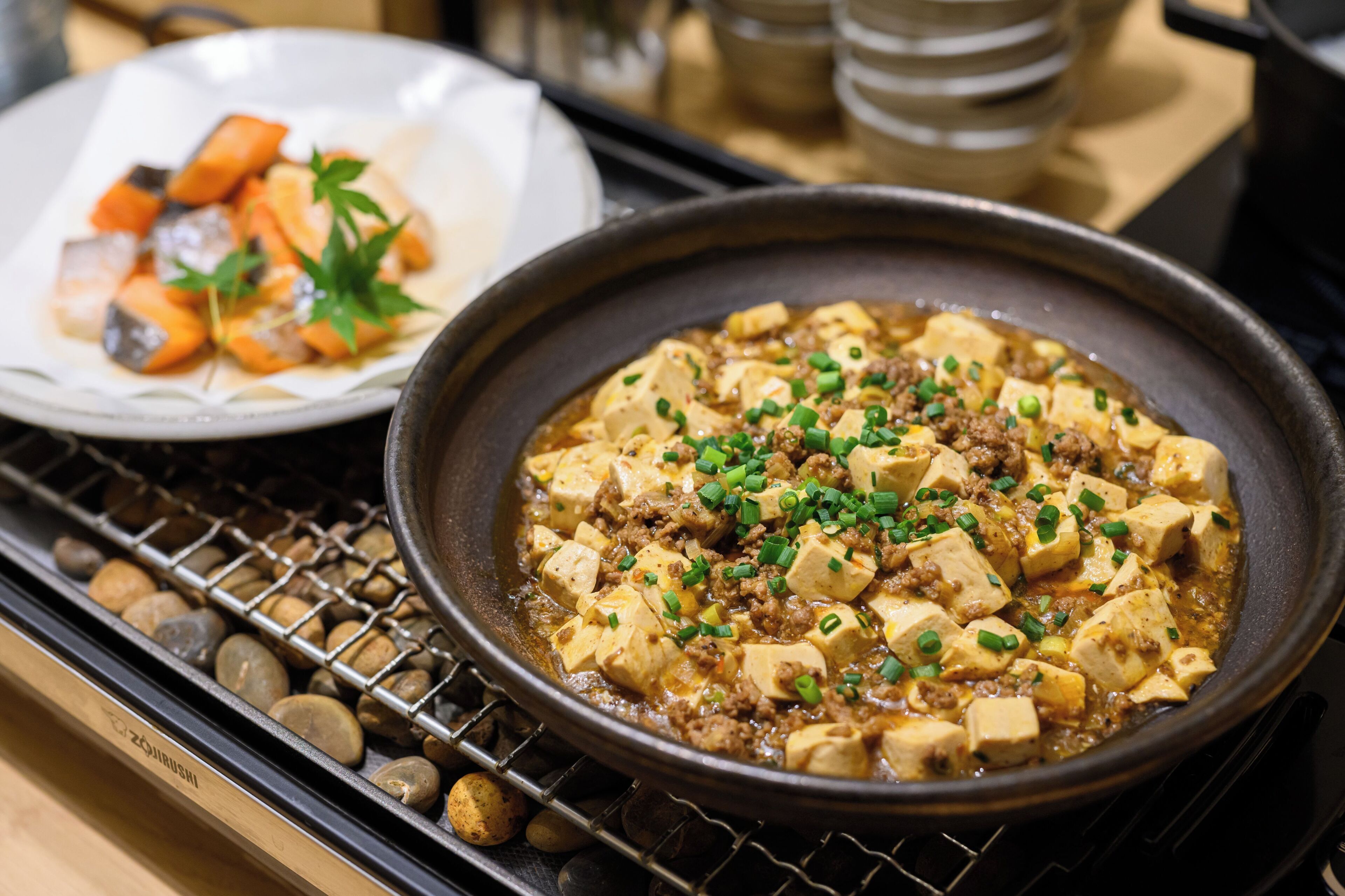 Un plato de olla caliente con tofu y carne, adornado con cebollines, servido en una sartén negra.