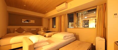 A hotel room with two beds, a small table, and a window with curtains.