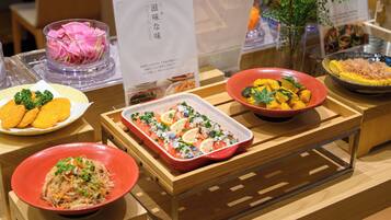 A variety of dishes displayed on a wooden table, including a dish with orange slices and herbs, a dish with yellow vegetables, and a dish with a red bowl.