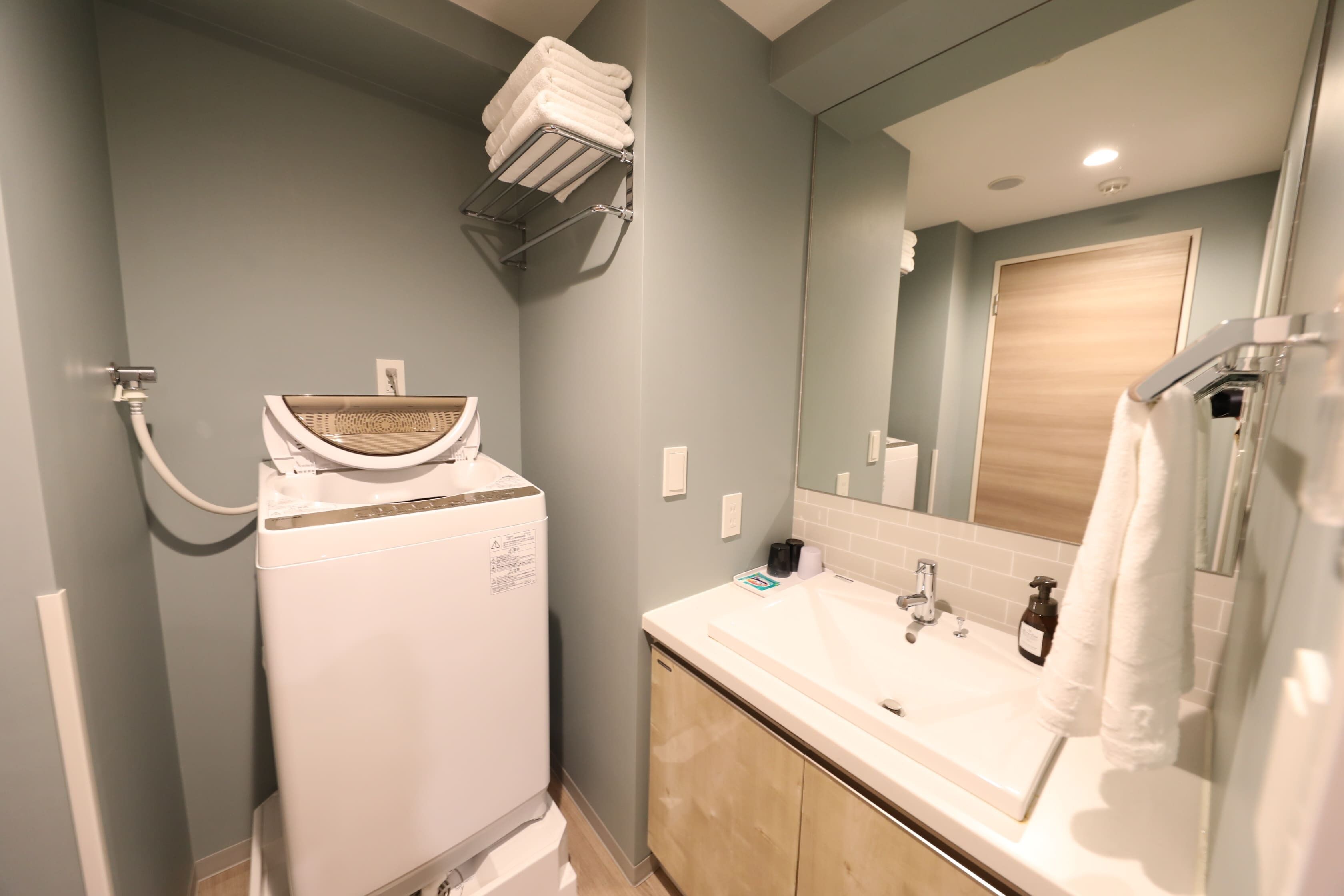 A bathroom with a white washing machine, a sink with a mirror, and a towel rack.