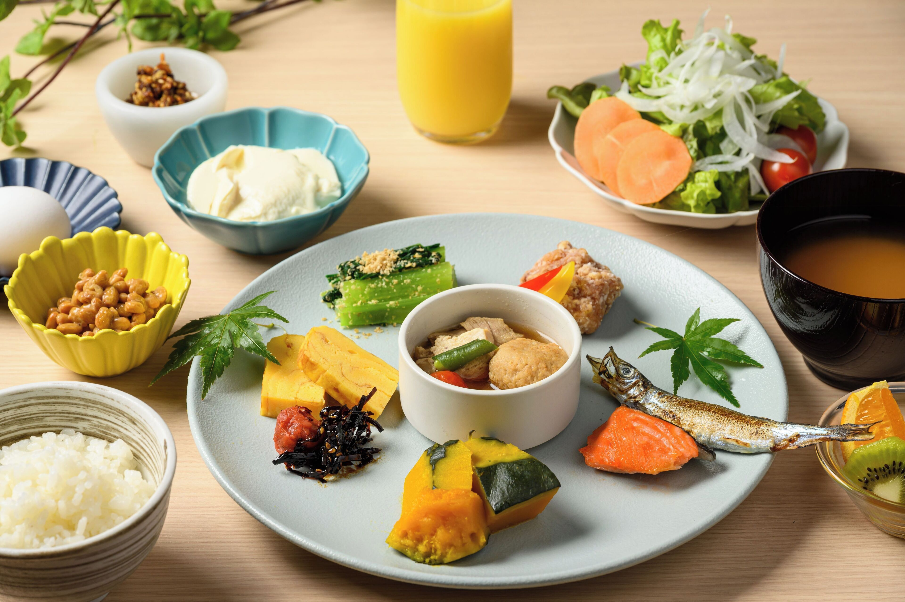 A variety of dishes including rice, vegetables, and fish on a plate, with bowls of side dishes and a glass of juice.