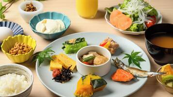 A variety of dishes including rice, vegetables, and fish on a plate, with bowls of side dishes and a glass of juice.