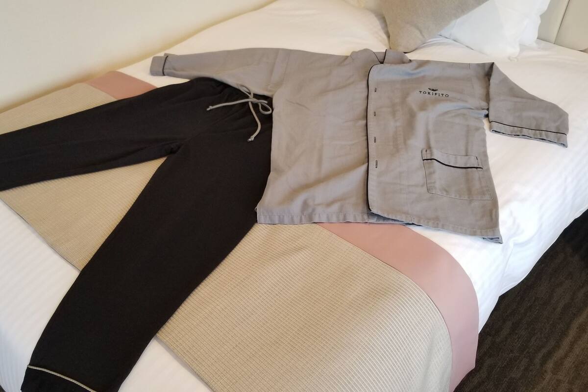 Un lit bien fait, avec une chemise grise, un pantalon noir et une serviette beige.