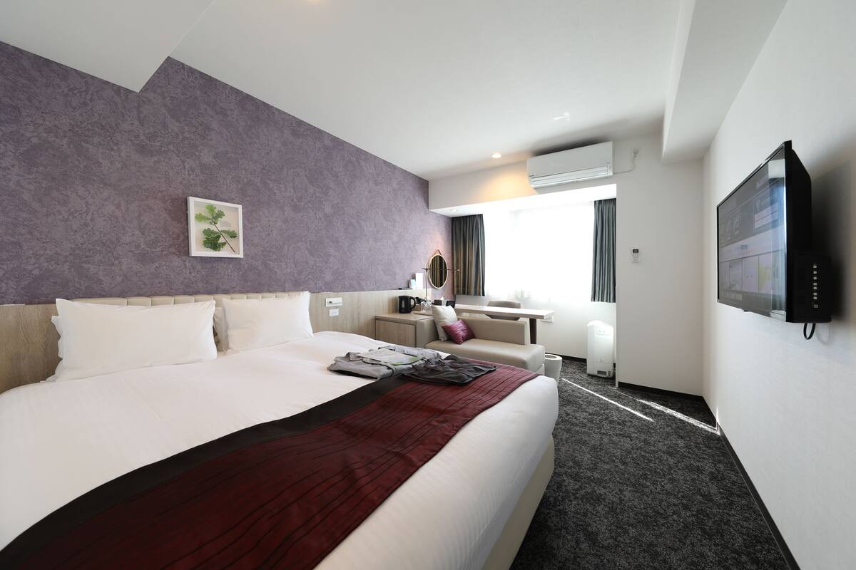 Une chambre d’hôtel avec un grand lit, un bureau, une chaise, une télévision et une fenêtre avec des rideaux.