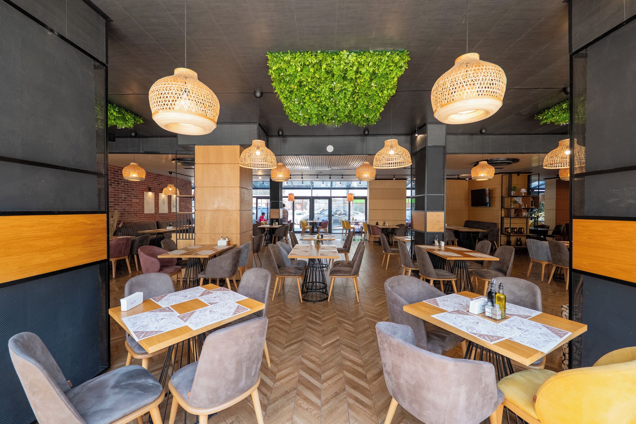 Un interior de restaurante moderno con mesas de madera, sillas tapizadas en gris y lámparas de mimbre colgantes.