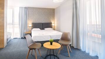 Quarto de hotel com uma cama, duas cadeiras, uma mesinha com uma planta e uma mesa de cabeceira com abajur.
