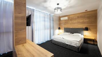 A modern hotel room with a wooden headboard, a bed with white linens, a bedside table, and a wall-mounted TV.